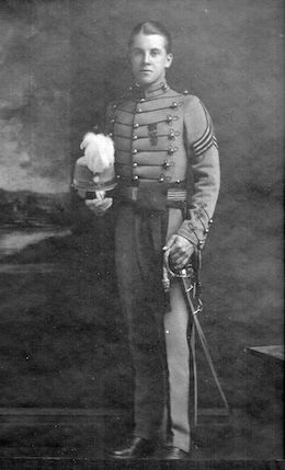 Black and white image of Hugh F. McCaffery standing in PMC uniform with a hat in one hand and a sword in the other. 